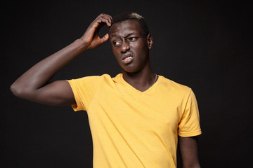 Preoccupied young african american man guy in yellow t-shirt posing isolated on black background studio portrait. People emotions lifestyle concept. Mock up copy space. Put hand on head looking aside.