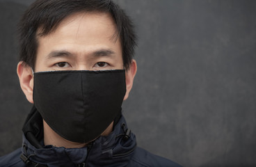 The face of Asian man wearing cloth mask to prevent PM 2.5 dust and smog germs, toxic fumes, and dust, Prevention of bacterial infection Corona virus or Covid 19 on the black background.