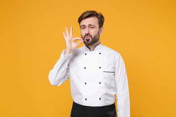 Young bearded male chef cook or baker man in white uniform shirt posing isolated on yellow wall background studio portrait. Cooking food concept. Mock up copy space. Making okay taste delight sign.