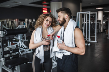 Beautiful young sports people are holding bottles of water, towel on back smiling during break time