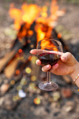 a glass of red wine in a female hand on a background of fire