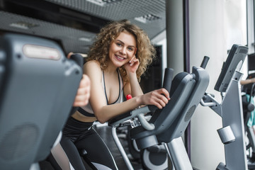 Fototapeta na wymiar Attractive young woman trainer running on treadmill in gym. Slim girl jogging in fitness club, smiling at camera. Healthy lifestyle concept, cardio training