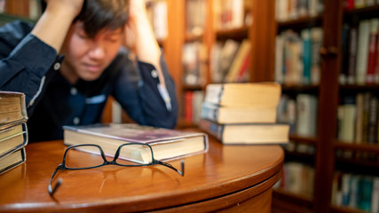 Smart Asian man university student feeling stressed and anxious while reading book by vintage...