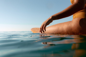 Midsection of woman sitting on surfboard