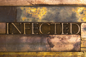 Photo of real authentic typeset letters forming Infected text on vintage textured grunge copper background