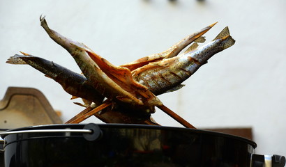 Räucherfisch. Auf Holzspießen gesteckte Forellen werden auf Grill geräuchert
