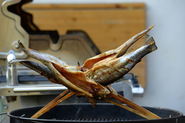 Räucherfisch. Auf Holzspießen gesteckte Forellen werden auf Grill geräuchert