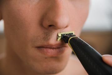 young man shaves off his mustache with a trimmer