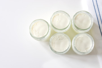 Homemade milk yogurt in glass jars on a white table. Top view, copyspace. Cooking at home during the COVID-19 quarantine
