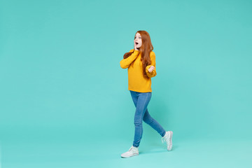 Shocked young redhead woman girl in yellow sweater posing isolated on blue turquoise wall background studio portrait. People lifestyle concept. Mock up copy space. Looking aside, put hand on cheek.