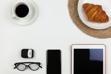 Modern working space of freelancer. Smartphone, coffee, tablet, croissant, glasses, headphones in case on white background, copy space, flat lay. Business breakfast, work from home, stay home concept