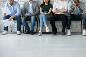 Close up of bored diverse multiracial job candidates sit in queue line feel anxious wait for...