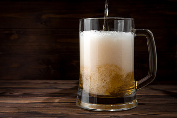 Light beer is poured into a mug on a wooden table. Beer in a mug.