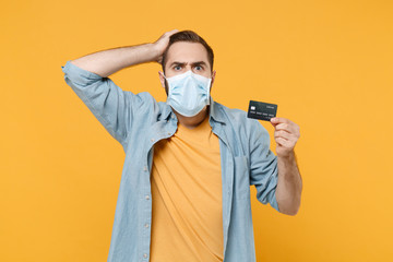 Fototapeta na wymiar Shocked young man in sterile face mask posing isolated on yellow background in studio. Epidemic pandemic coronavirus 2019-ncov sars covid-19 flu virus concept. Hold credit bank card put hand on head.