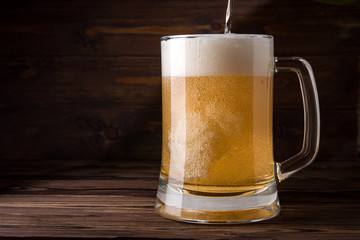 Light beer is poured into a mug on a wooden table. Beer in a mug.