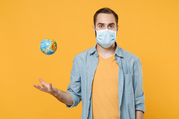 Young man in sterile face mask posing isolated on yellow background studio portrait. Epidemic pandemic spreading coronavirus 2019-ncov sars covid-19 flu virus concept. Throwing up Earth world globe.