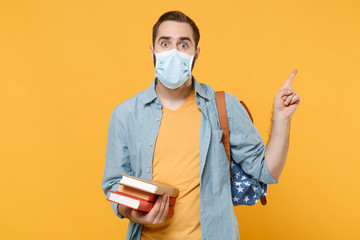 Shocked young man in sterile face mask with backpack posing isolated on yellow background. Epidemic...