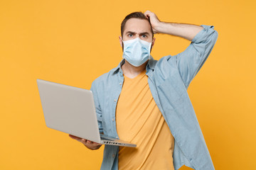 Preoccupied young man in sterile face mask posing isolated on yellow background. Epidemic pandemic...