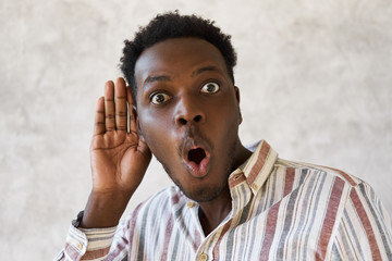 Isolated image of funny young dark skinned man having curious look eavesdropping behind door,...