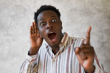 Omg, Wow. Portrait of shocked young African news monger raising fore finger and opening mouth...