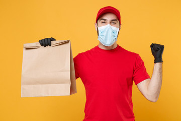 Delivery man employee in red cap blank t-shirt uniform mask glove hold craft paper packet with food isolated on yellow background studio Service quarantine pandemic coronavirus virus 2019-ncov concept