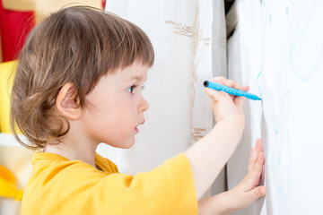 little child draws on a white board with a felt-tip pen. Home activities in self-isolation