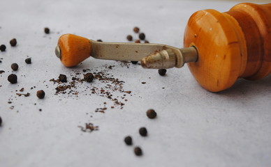 Old wooden Pepper Mill and Peppercorns on a gray background. Close up view.