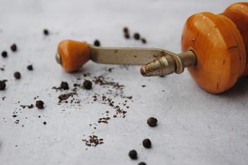 Wooden Pepper Mill with a metal handle on a gray background. Peppercorns around the pepper mill,...