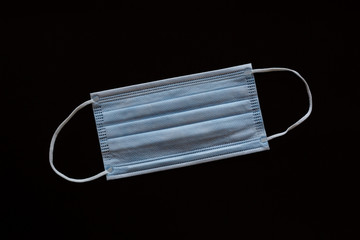 Medical mask light blue in the hands with black gloves on a black background, protection