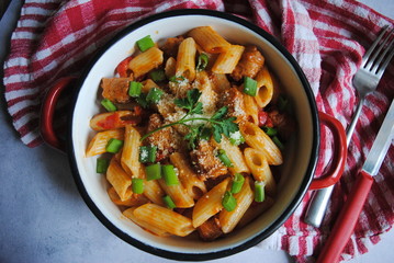 Penne Pasta with Sausages and Vegetables sprinkled with slices of Green onions and Parmesan, fresh parsley leaf in the middle. Top view.