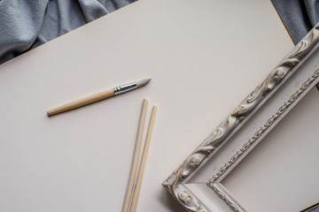 Space for creativity and art: brushes, vintage frame and blank paper on blue fabric.