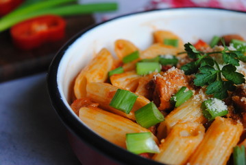 Pasta with sausages, green onions, and peppers in an enamel pot, decorated with basil. Close up view.