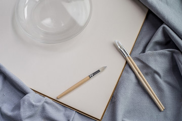 Creative space: cristal jar, brushes and blank paper on blue fabric.