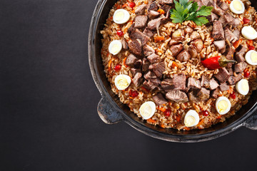 Close-up of pilaf with sliced meat, garlic decorated with quail eggs. Family portion. Uzbek traditional dish plov. Dark background.