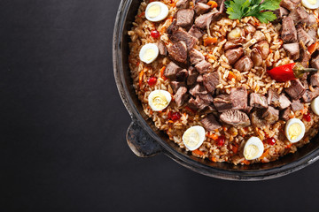 Close-up of pilaf with sliced meat, garlic decorated with quail eggs. Family portion. Uzbek traditional dish plov. Dark background.