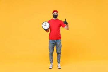 Delivery man in red cap blank t-shirt uniform sterile face mask gloves isolated on yellow background studio Guy employee working courier hold clock Service pandemic coronavirus virus 2019-ncov concept