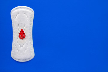 Menstrual pad with red sparkles in the form of a drop of blood on a blue background, top view, miniature of the menstrual period
