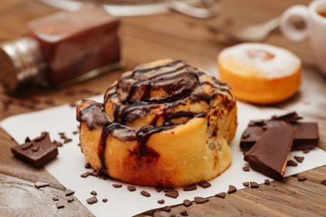 bun with chocolate and cinnamon on a wooden table. Next to pieces of chocolate, a donut, a jar of cinnamon and snnabon
