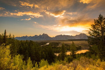 Golden sunlight reflects off the Snake River in Grand Tetons National Park, as the sun sets behind the Teton Range.