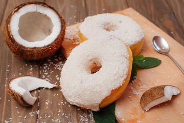 two large coconut donuts on a cutting board with mint leaves and coconut pieces laid out nearby