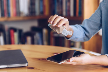Coronavirus concept. Girl working from home put antiseptic gel on her mobile. Global call to stay...