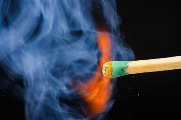 A lighted match with smoke and sparks on a black background, macro.