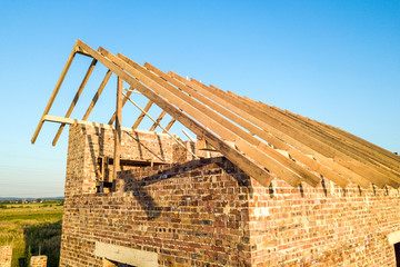 Unfinished brick house with wooden roof structure under construction.