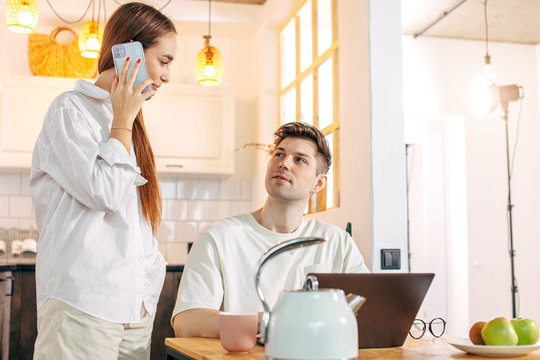 Caucasian Woman Talk On Phone While Her Husband Work On Laptop. Everyone In The Family Busy With Their Own Business. Freelance During Quarantine, Coronavirus All Over The World. Stay At Home