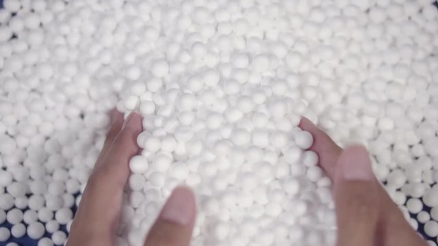 Hand holding white polystyrene foam beads ball drop from Styrofoam machine for fragile stuff packaging box on blue modern luxury background for decoration