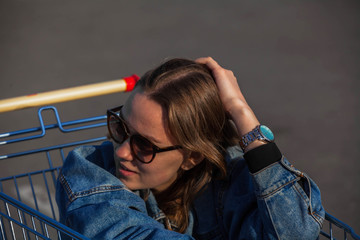 Girl with glasses sitting in a grocery cart in the parking lot