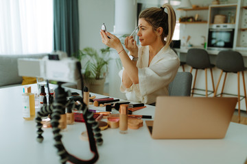 Photo of beautiful woman with ponytail applying makeup while looking at handy mirror. Young woman...