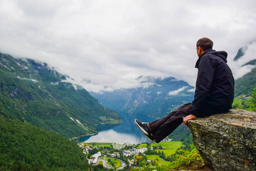 Male tourist sitting on the cliff edge near Flydalsjuvet Viewpoint. Travel Norway.