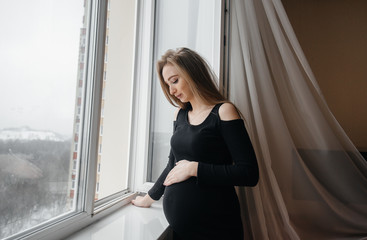 A pregnant girl is breathing fresh air from the window