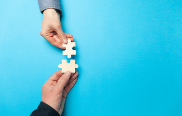 Two hands connect puzzles on a blue background. Cooperation and teamwork in business. Collaboration people for success. - obrazy, fototapety, plakaty